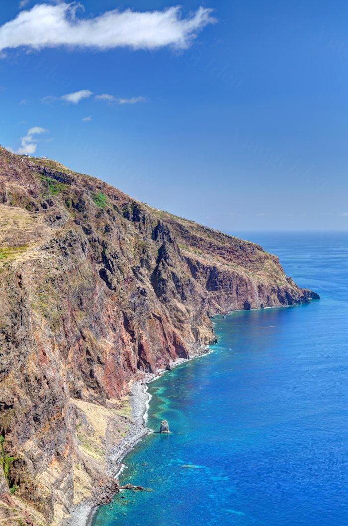 Costa rocciosa con vegetazione bassa e mare blu sotto un cielo sereno