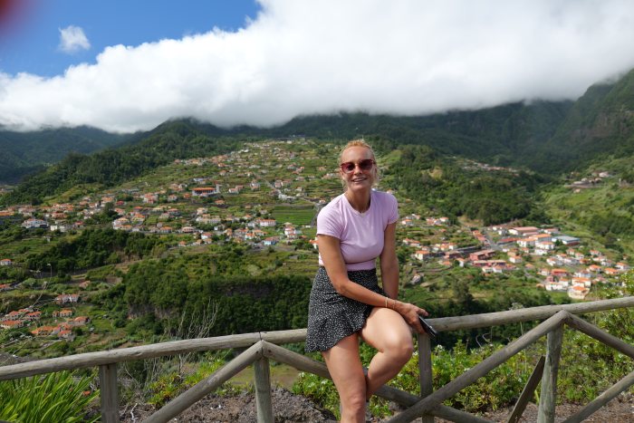 Donna sorridente appoggiata a una ringhiera con vista su un paese in collina