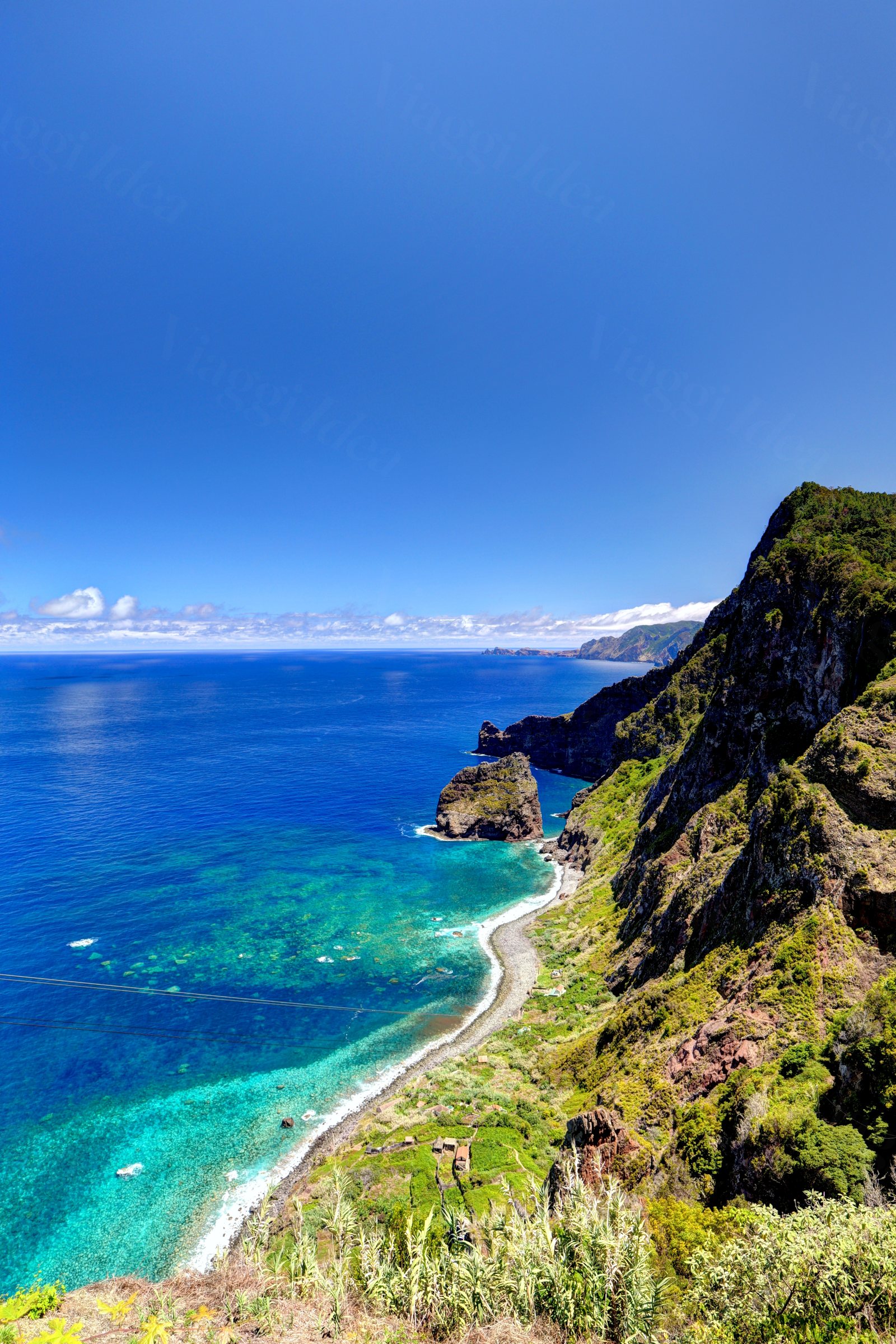 Baia con mare turchese, spiaggia di sassi e montagne verdi